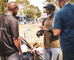 3 men speaking, one with a camera